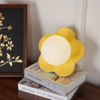 Standing on a stack of books beside a framed artwork, this Clérachic wall light in yellow sits unlit.