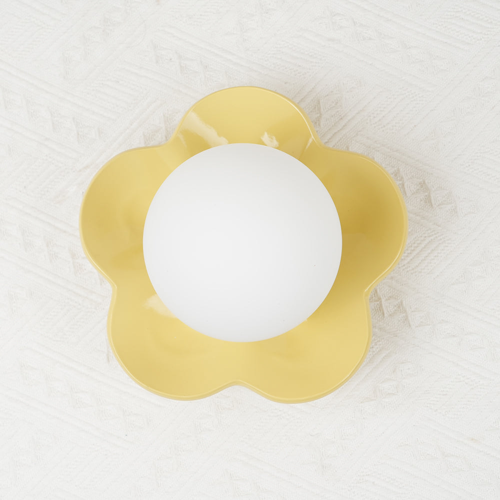 Close studio shot of this Clérachic wall light in yellow, its ball lit against a textured pale backdrop.