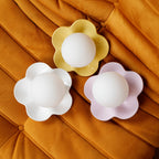 Three of these Clérachic wall lights lie flat on an orange velvet cushion, in yellow, white and pink.