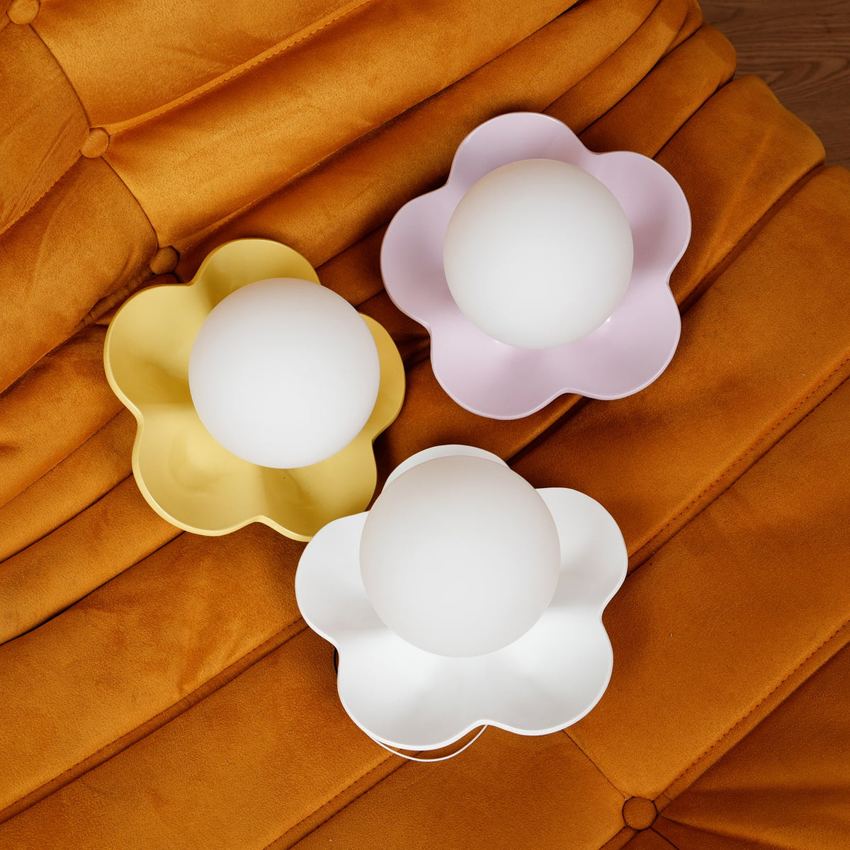 Three of these Clérachic wall lights sit on an orange velvet cushion, in gold, lilac and white.