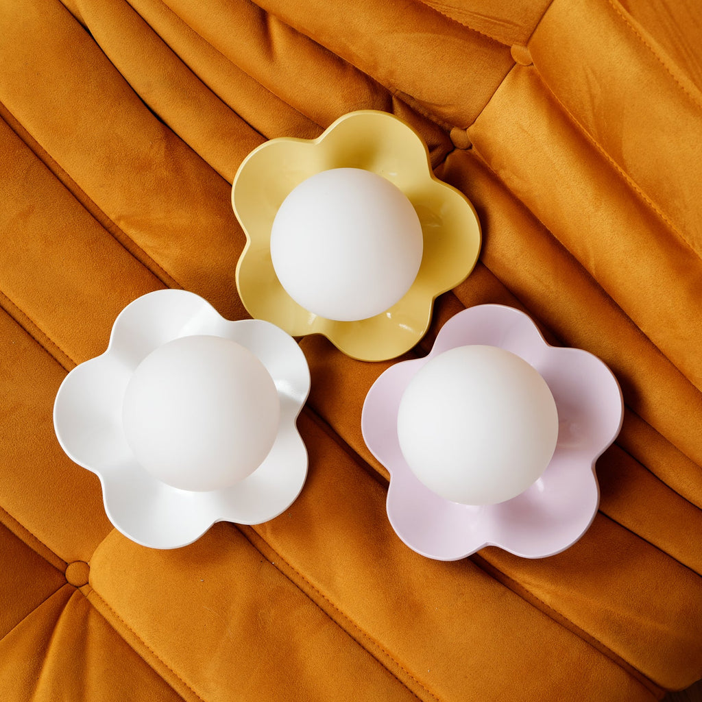 Three of these Clérachic wall lights are grouped on an orange velvet cushion, in yellow, white and pink.