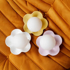 Three of these Clérachic wall lights are grouped on an orange velvet cushion, in yellow, white and pink.