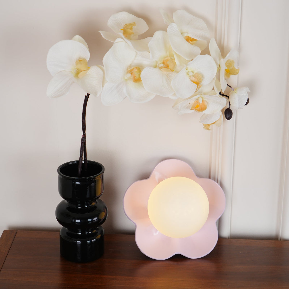 Close view of this Clérachic wall light in pink on the table, the black orchid vase just behind it.
