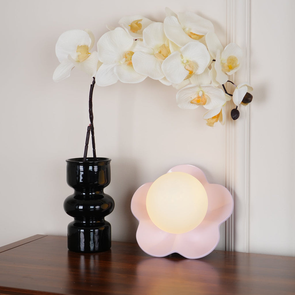Set on a wooden table beside a black vase of white orchids, this Clérachic wall light in pink sits unlit.