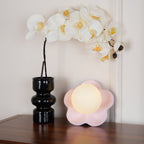 Set on a wooden table beside a black vase of white orchids, this Clérachic wall light in pink sits unlit.