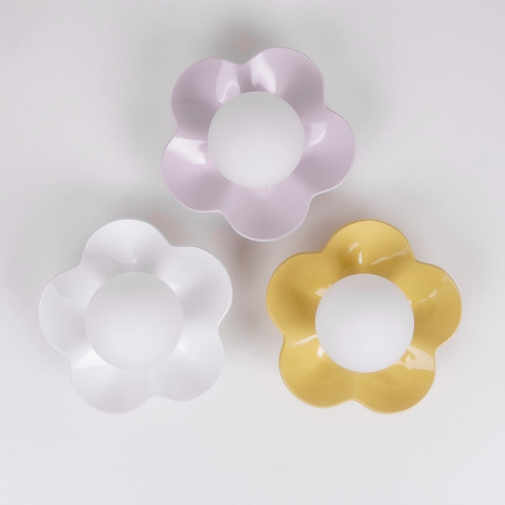 Three colour options of this Clérachic wall light shown together, in lilac, white and yellow, on a plain backdrop.