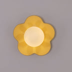 Close studio shot of this Clérachic wall light in yellow, its petals unlit against a plain grey backdrop.