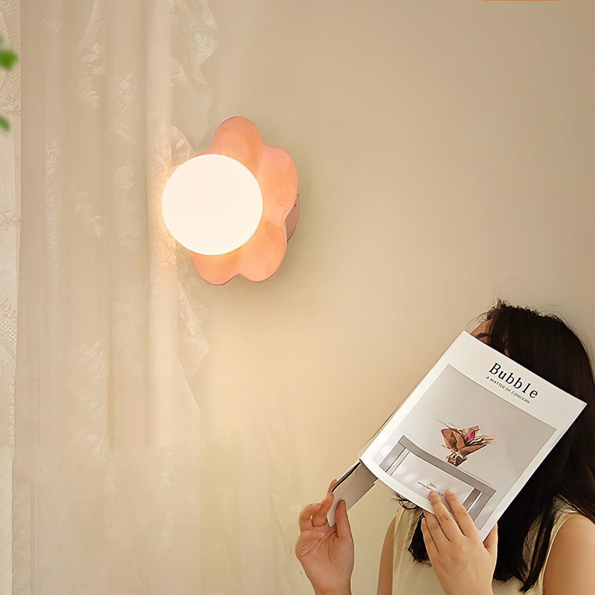 Partly hidden by a woman reading a magazine, this Clérachic wall light in pink glows on the wall behind her.