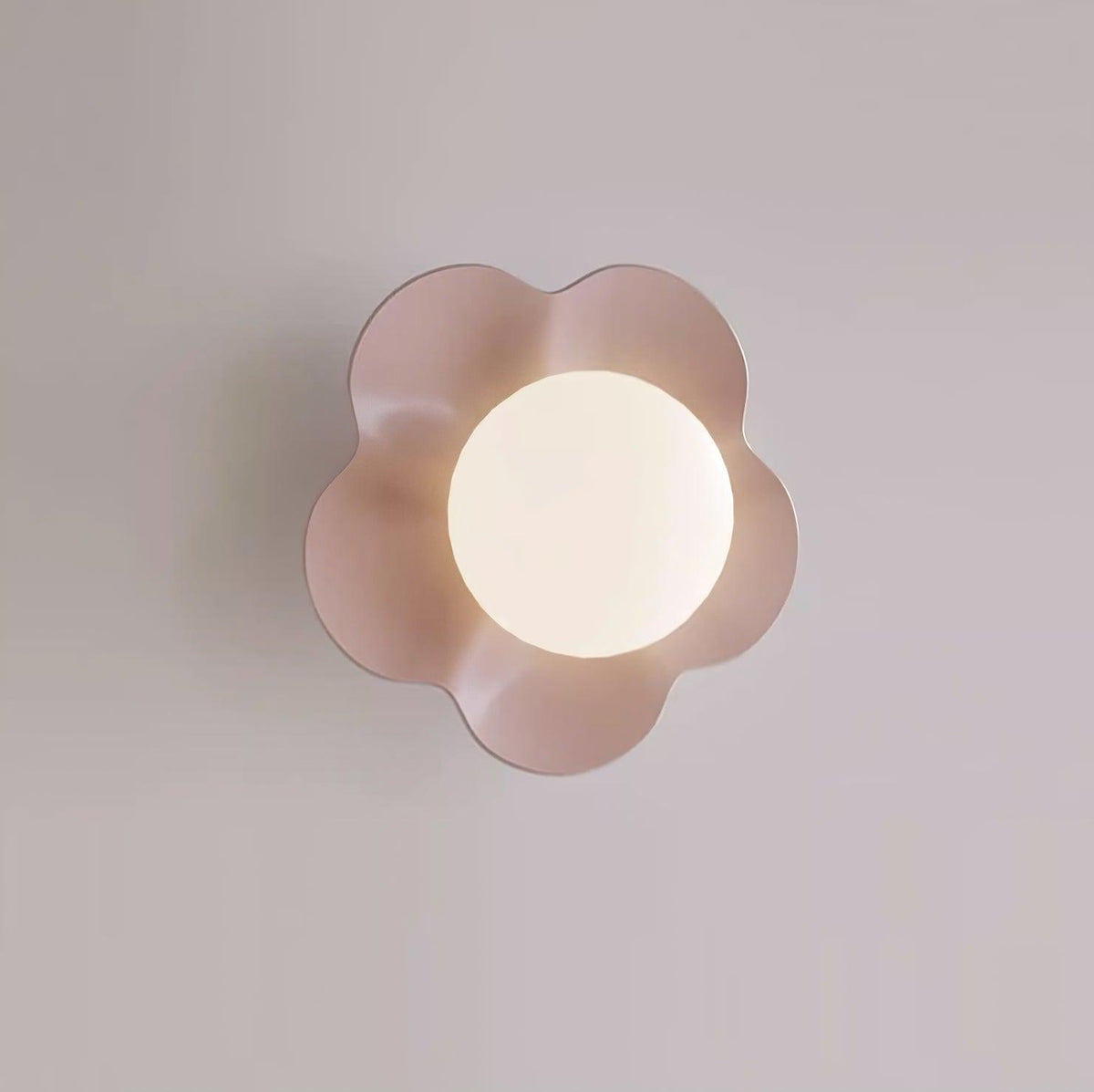 Close studio shot of this Clérachic wall light in a blush tone, its ball lit against a lavender backdrop.