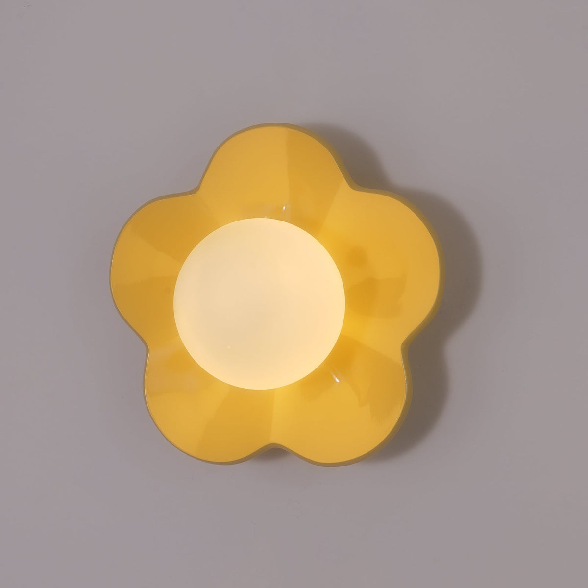 Seen straight on, this Clérachic wall light in a deeper golden yellow sits unlit against a plain backdrop.
