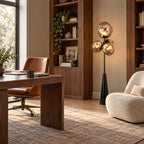 Clérachic floor lamp lit beside a walnut desk and leather chair in a home office, its smoke-glass globes clustered above a slim black stem.