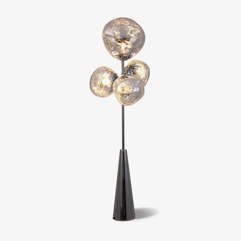 Clérachic floor lamp lit against a plain white backdrop, a soft shadow beneath the base and warm light filling its glass globes.