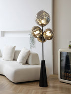 Clérachic floor lamp glowing in a pale, minimalist room, its smoke-glass globes rising beside a boucle sofa and a black bar cabinet.