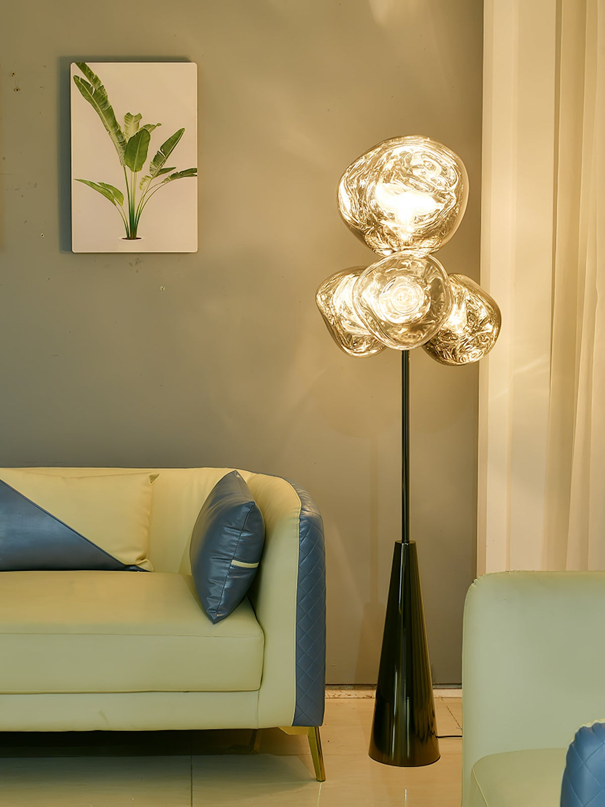 Smoke-glass globes glow beside a botanical print and pale sofa with blue cushions, this Clérachic floor lamp warming a sage-green living room.