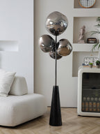 Unlit mirror-chrome globes on this Clérachic floor lamp reflect a cream boucle sofa and display shelving in a bright, minimalist room.