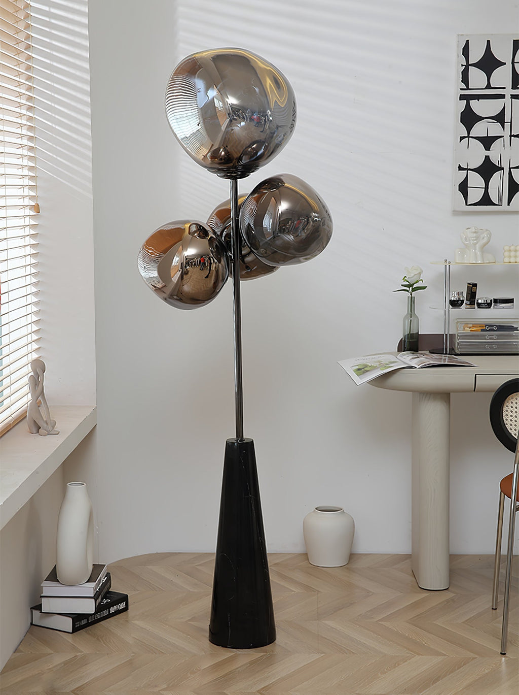 Clérachic floor lamp lit near a windowsill desk, its smoke-glass globes glowing beside a stack of books and a small ceramic vase.