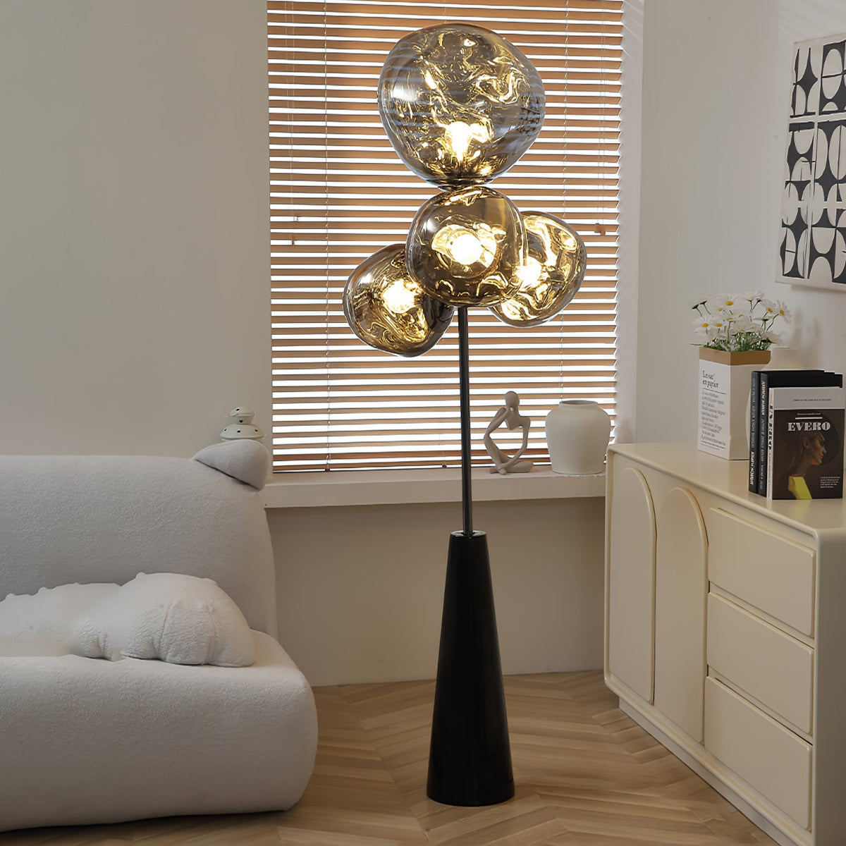 Striped window-blind light falls across a Clérachic floor lamp, its smoke-glass globes glowing beside a cream sideboard on a herringbone floor.