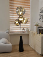 Clérachic floor lamp lit beside a cream sideboard and fresh flowers, warm wood-slat blinds filtering light across its smoke-glass globes.