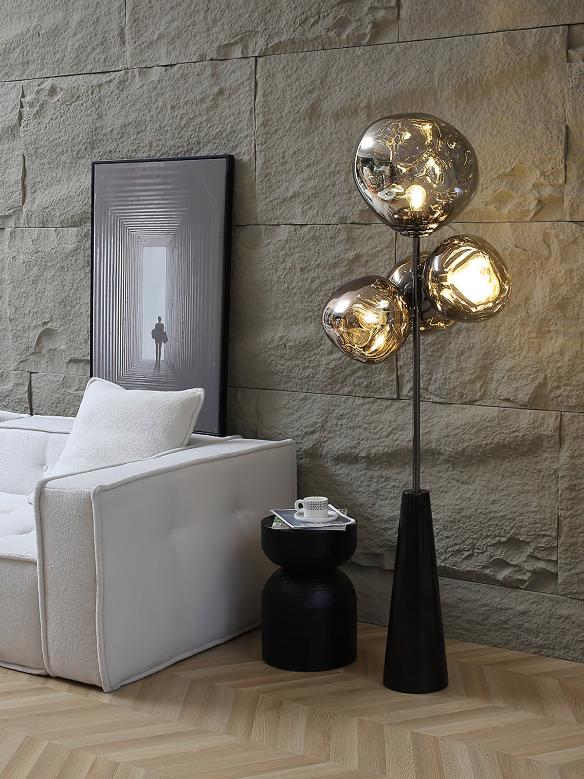 A closer crop of the stone accent wall scene, this Clérachic lamp's marbled glass globes glowing warmly beside a white sofa and artwork.
