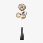 Clérachic floor lamp lit and cut out against a plain white background, its clustered smoke-glass globes glowing above the black base.