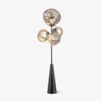 Clérachic glass-globe floor lamp glowing against a plain grey backdrop, four marbled smoke-glass globes on a black conical base.