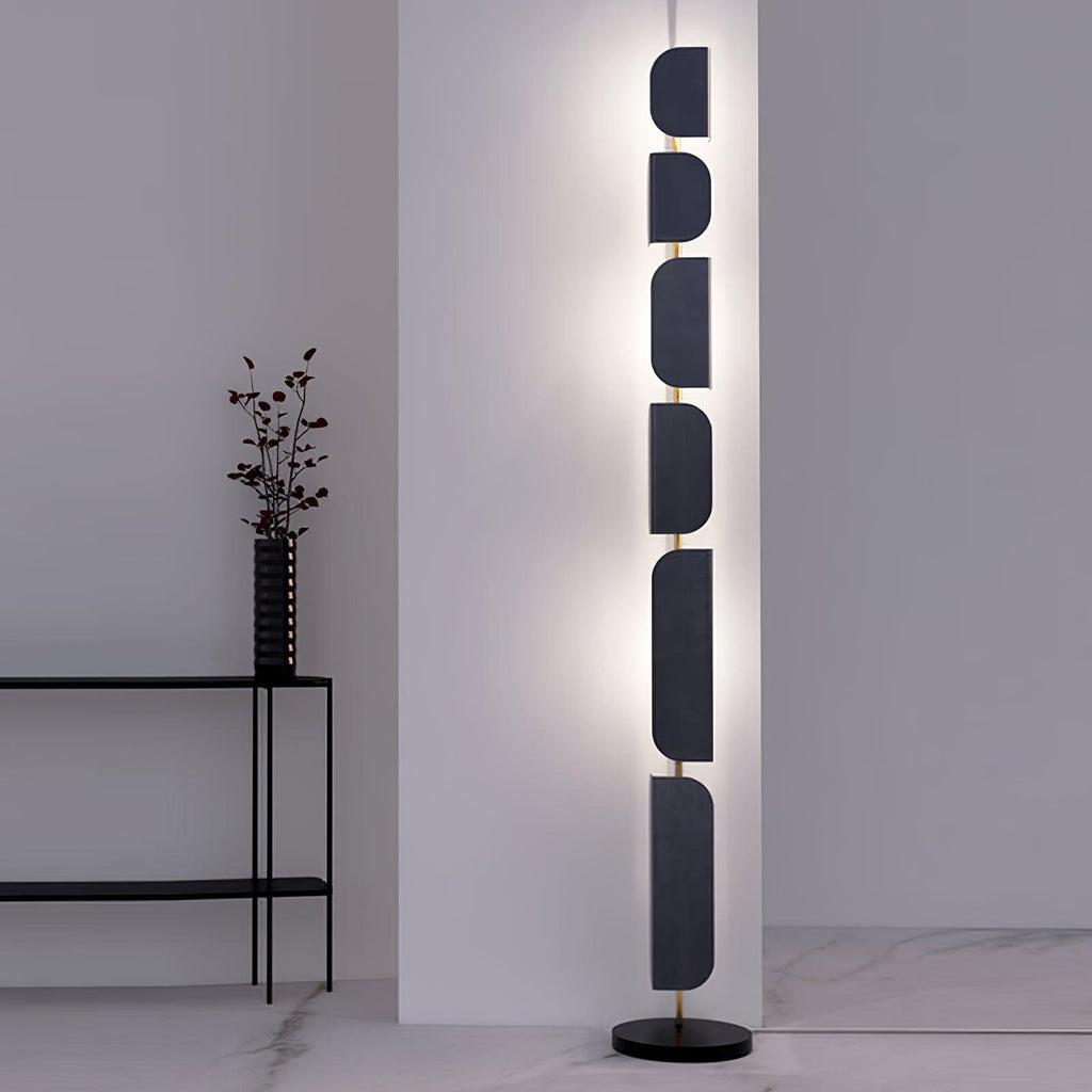 The Clérachic floor lamp glows beside a black side table holding a dark ridged vase with dried branches.