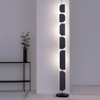 The Clérachic floor lamp glows beside a black side table holding a dark ridged vase with dried branches.