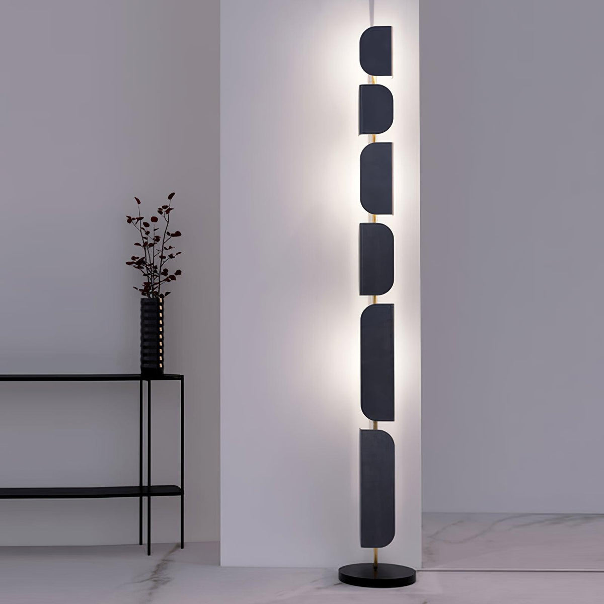 The Clérachic floor lamp glows beside a black side table holding a dark ridged vase with dried branches.