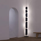 Full height view of the Clérachic floor lamp glowing beside a stairwell archway and a low wood bench.