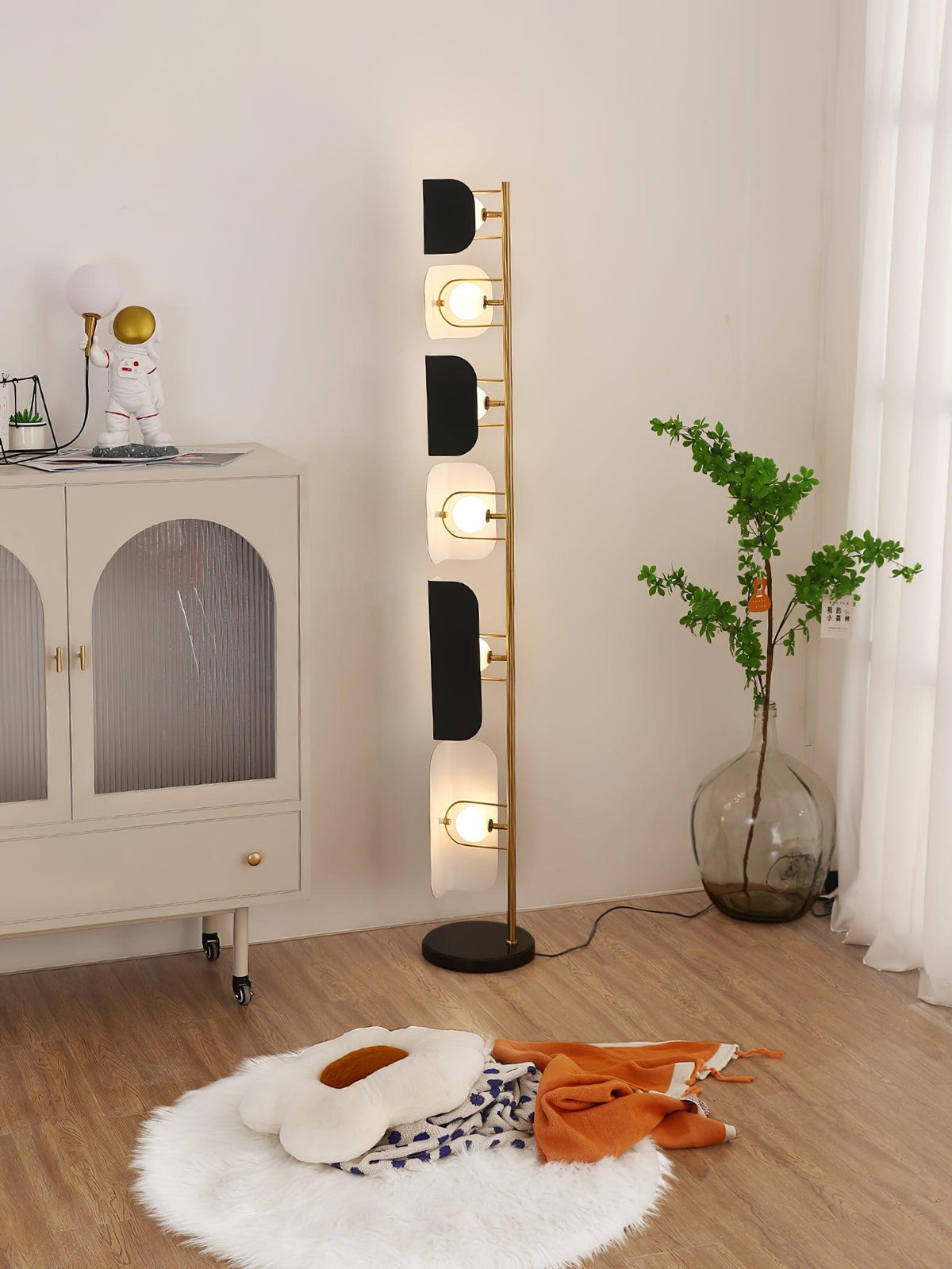 A small astronaut figurine sits atop the cabinet beside the glowing Clérachic floor lamp and a potted plant.