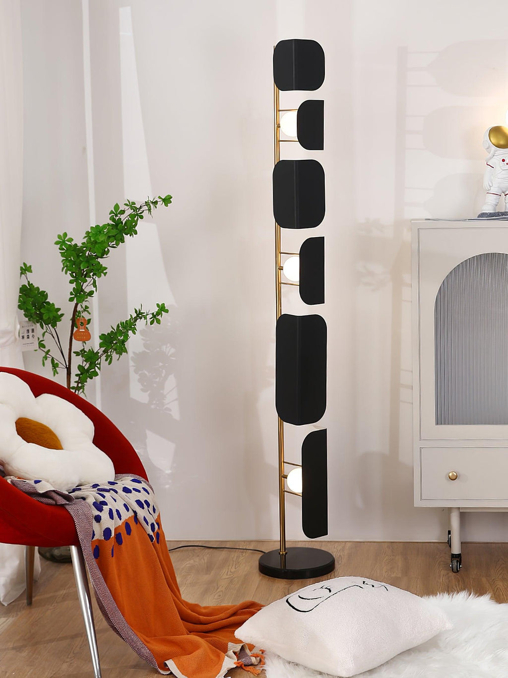 The Clérachic floor lamp lit beside the arched cabinet and red chair, an orange throw trailing onto the sheepskin rug below.