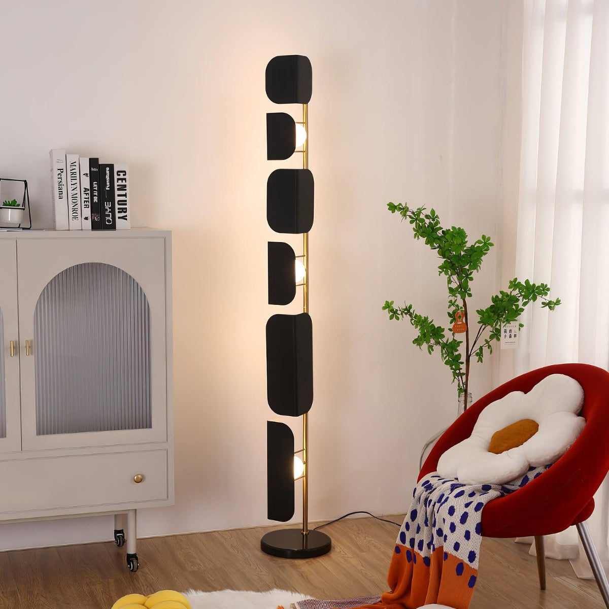 A Clérachic black glass floor lamp glows in a living room corner beside a cream arched cabinet, a red flower-shaped chair and a sheepskin rug.