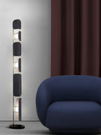 The Clérachic floor lamp stands beside a rounded navy armchair, a burgundy curtain hanging against the grey wall behind it.