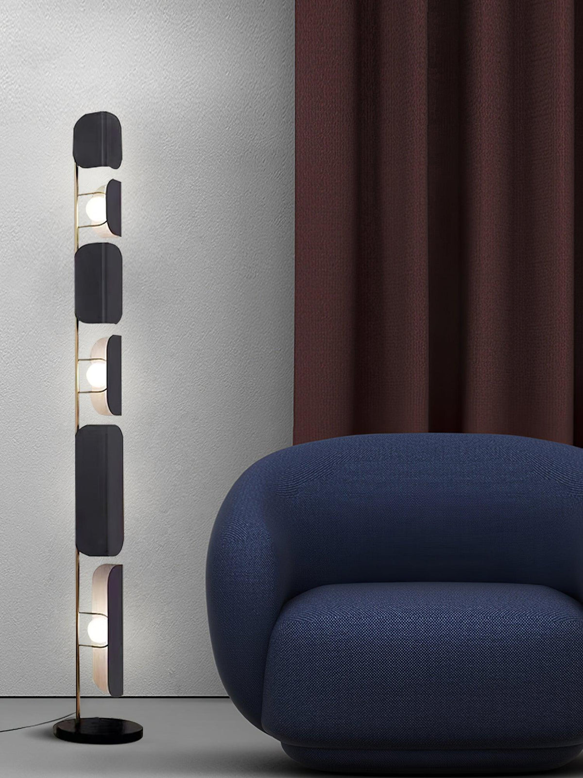 The Clérachic floor lamp stands beside a rounded navy armchair, a burgundy curtain hanging against the grey wall behind it.