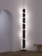 Near a stairwell archway, the Clérachic floor lamp casts a warm glow up the wall beside a low wood bench.