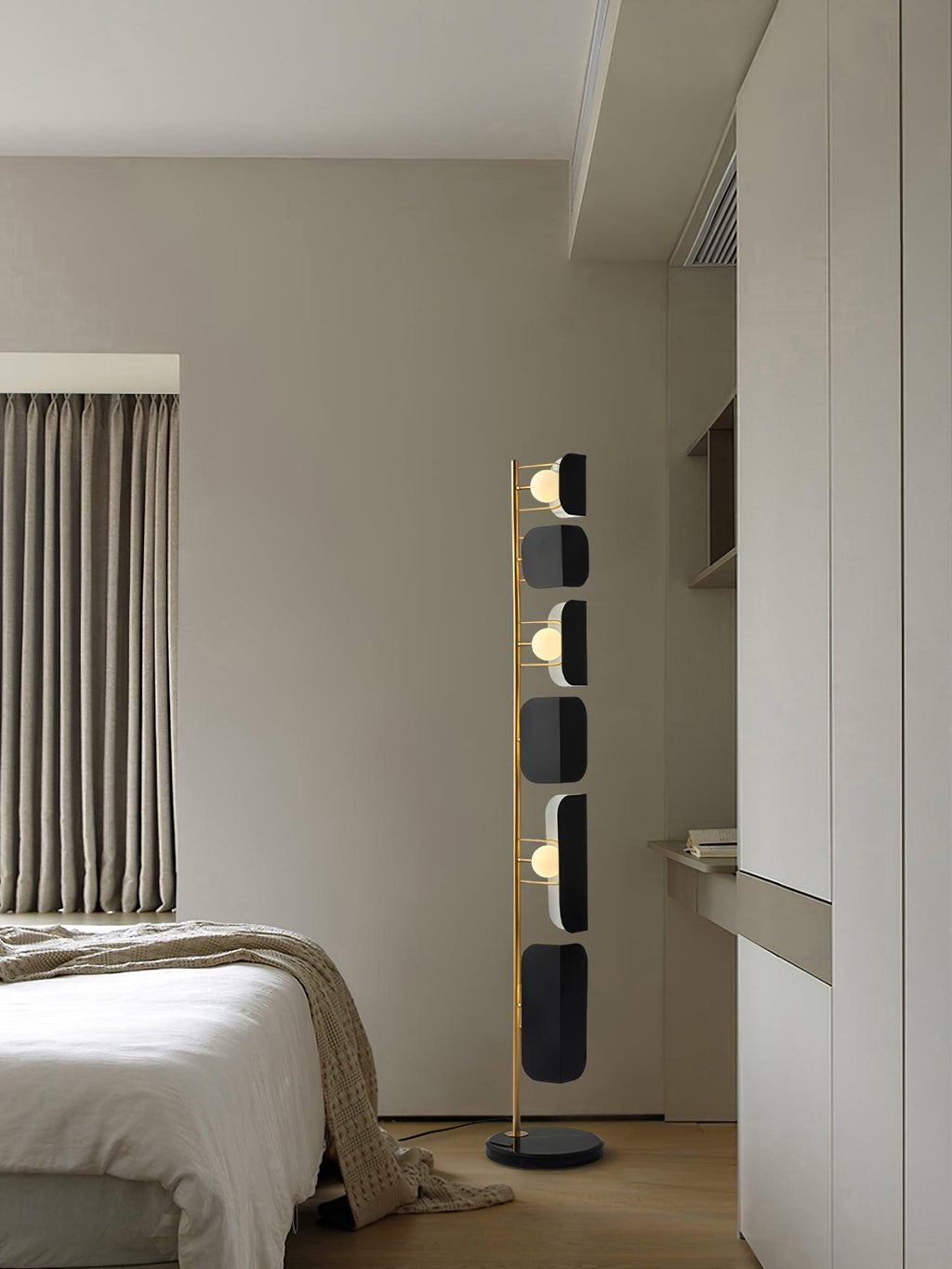 The Clérachic floor lamp stands in a bedroom corner against a cream curtain, its black glass panels lit softly.