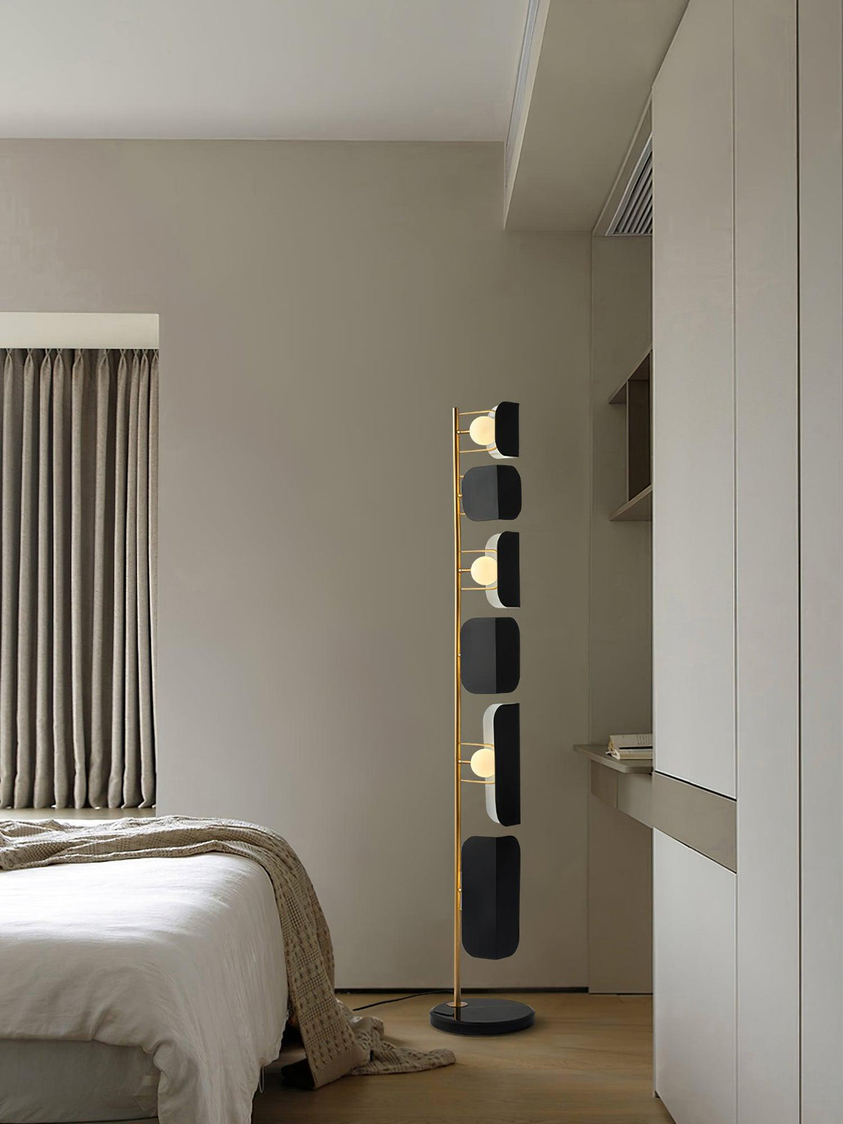 The Clérachic floor lamp stands in a bedroom corner against a cream curtain, its black glass panels lit softly.