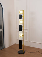Full-length view of the Clérachic floor lamp beside a mirrored archway, its black marble base and glowing glass panels both visible.
