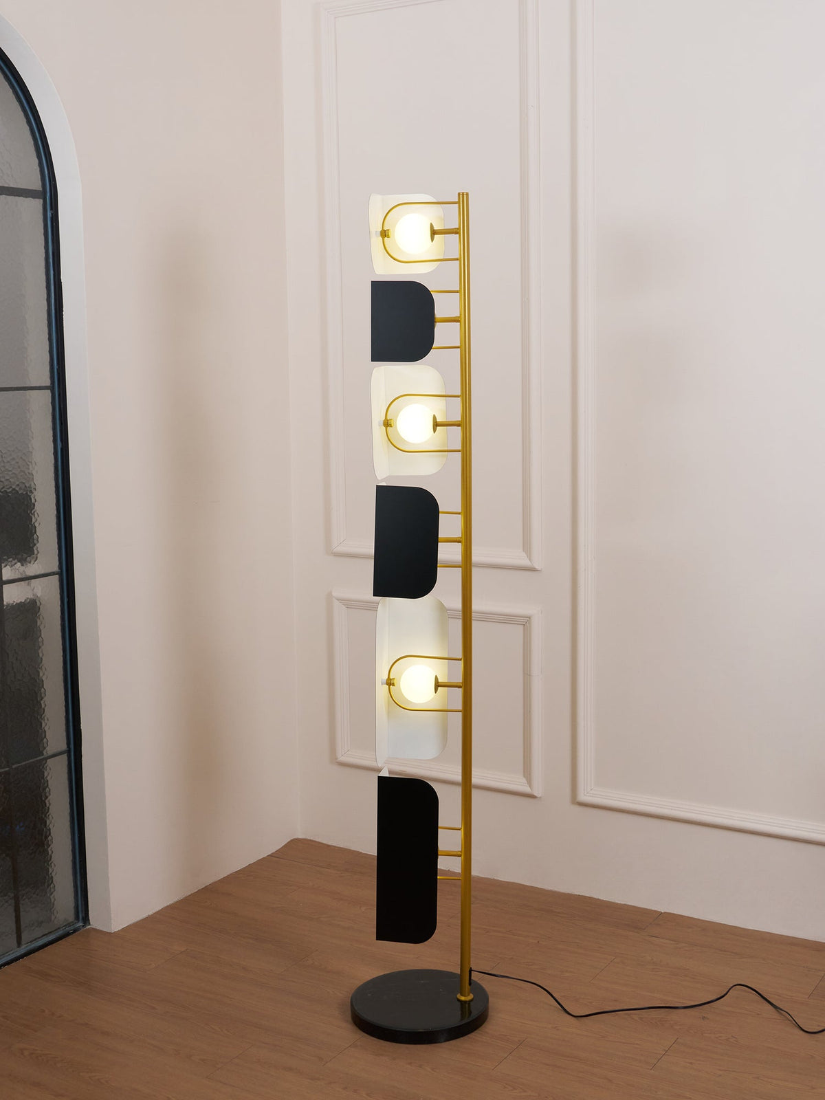 Full-length view of the Clérachic floor lamp beside a mirrored archway, its black marble base and glowing glass panels both visible.