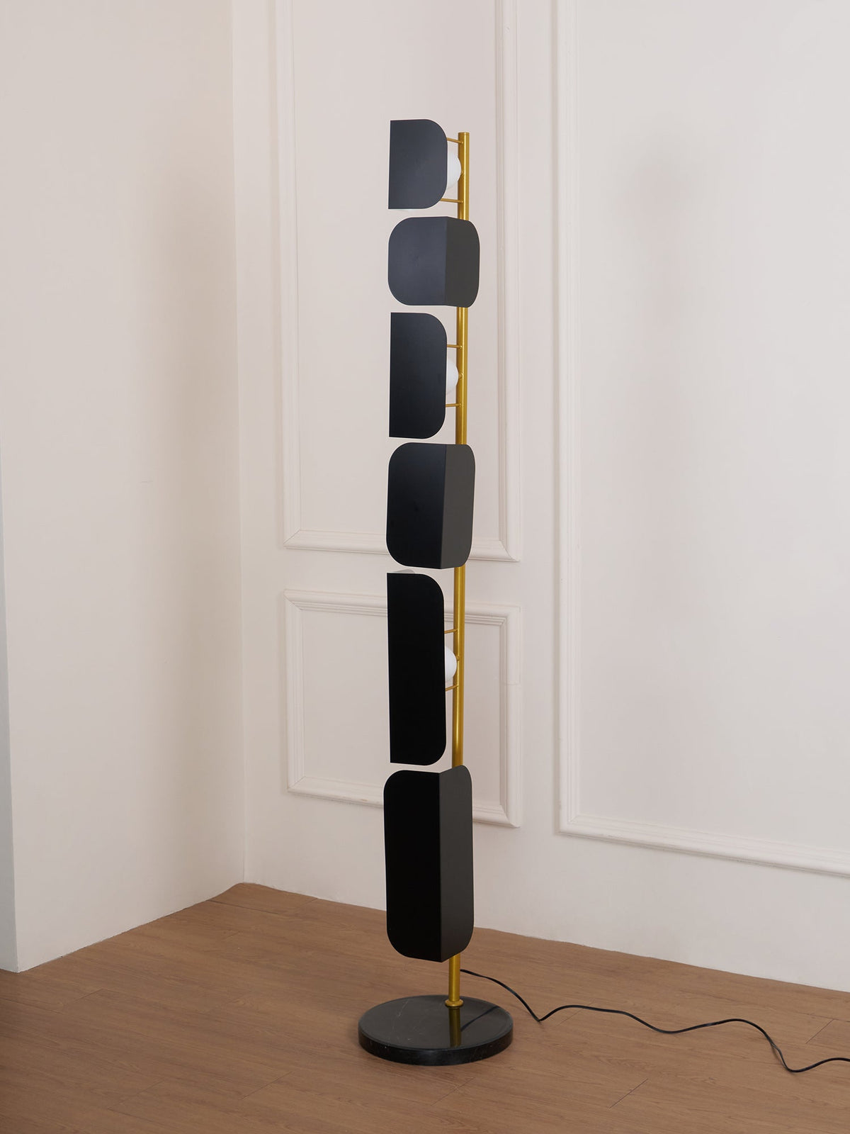 The Clérachic floor lamp's black marble base sits in a room corner, its power cord trailing across the wood floor.