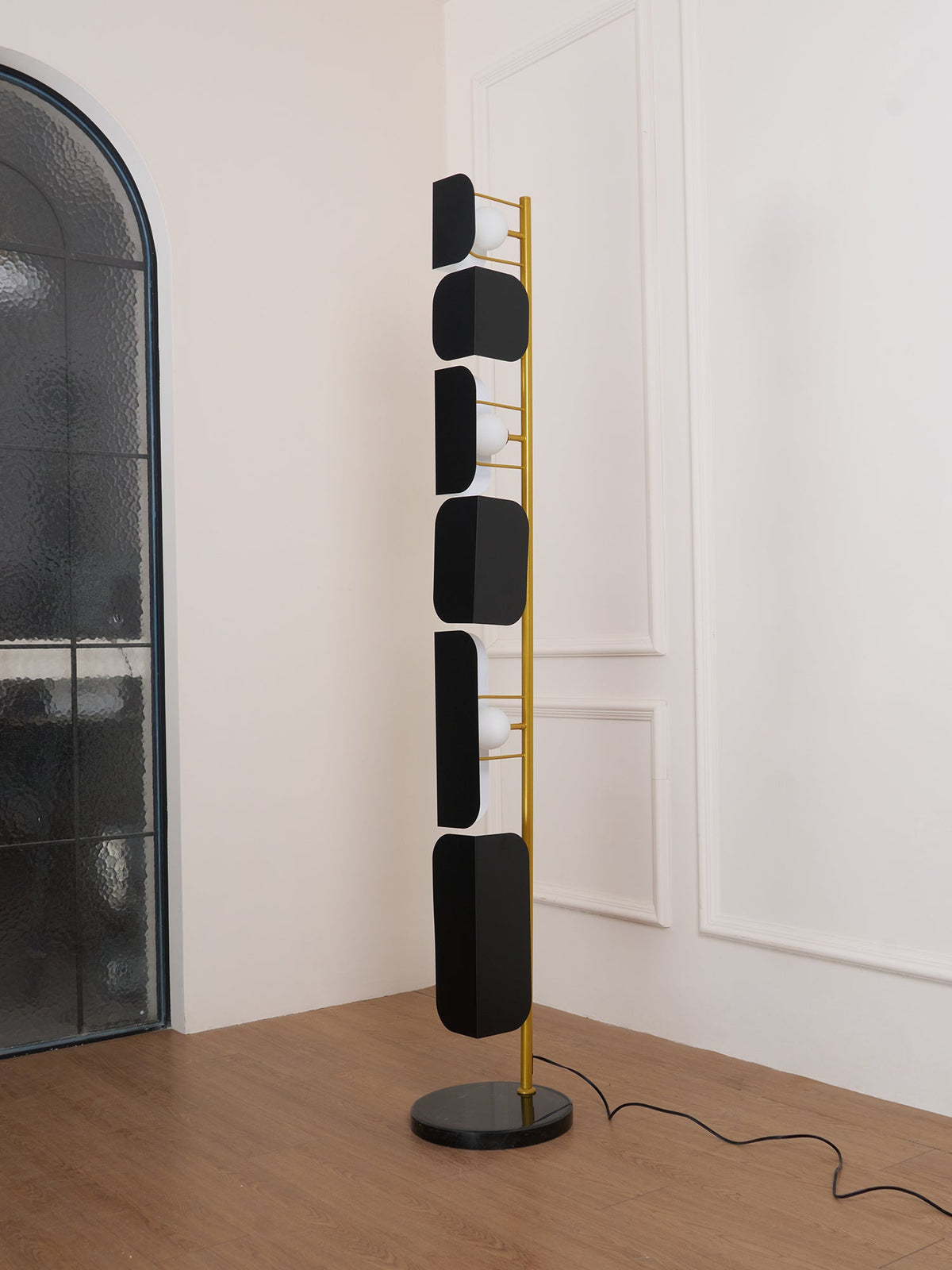 The Clérachic floor lamp stands near an arched frosted-glass door, its glass panels lit above the wood floor.