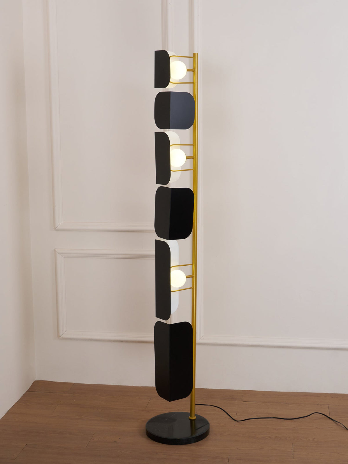 The Clérachic floor lamp against a plain beige wall, its round black marble base and gold pole shown clearly at floor level.