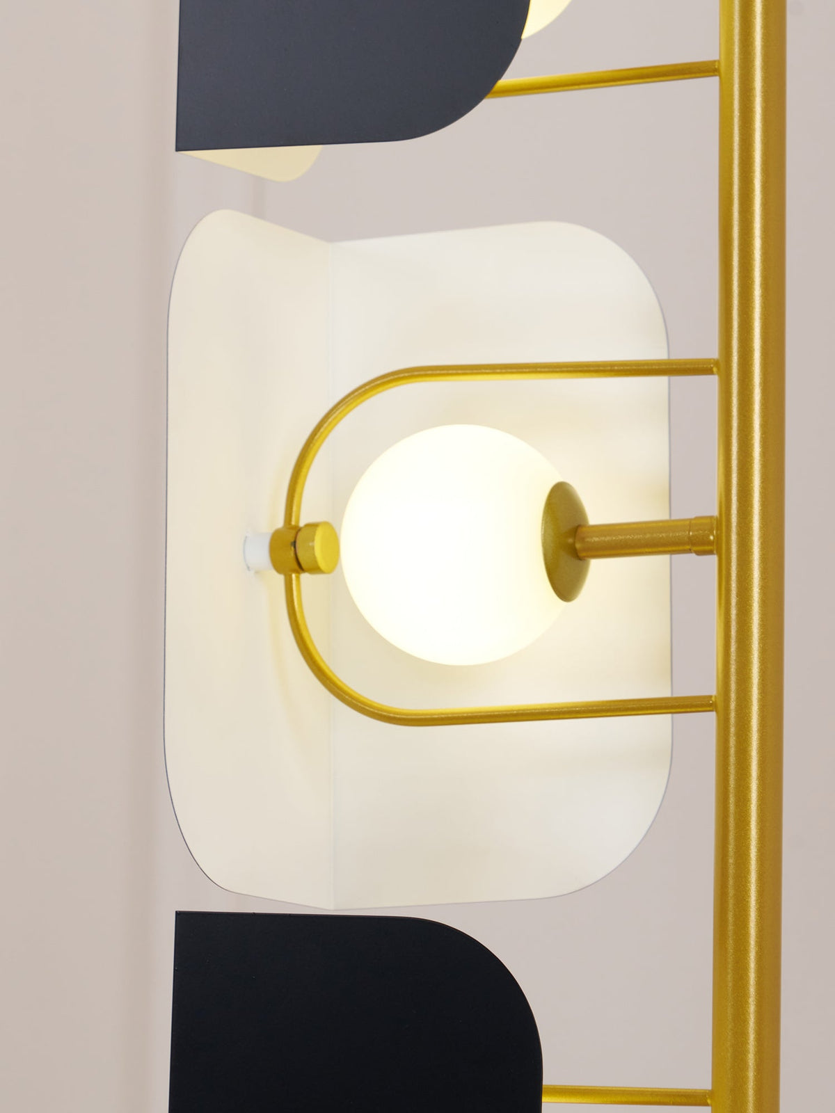 Macro detail of one lit opal glass globe seated in the Clérachic floor lamp's gold frame beside a black glass panel.