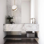 Above a marble vanity with brass tapware, a single pendant glows from this Clérachic fixture.