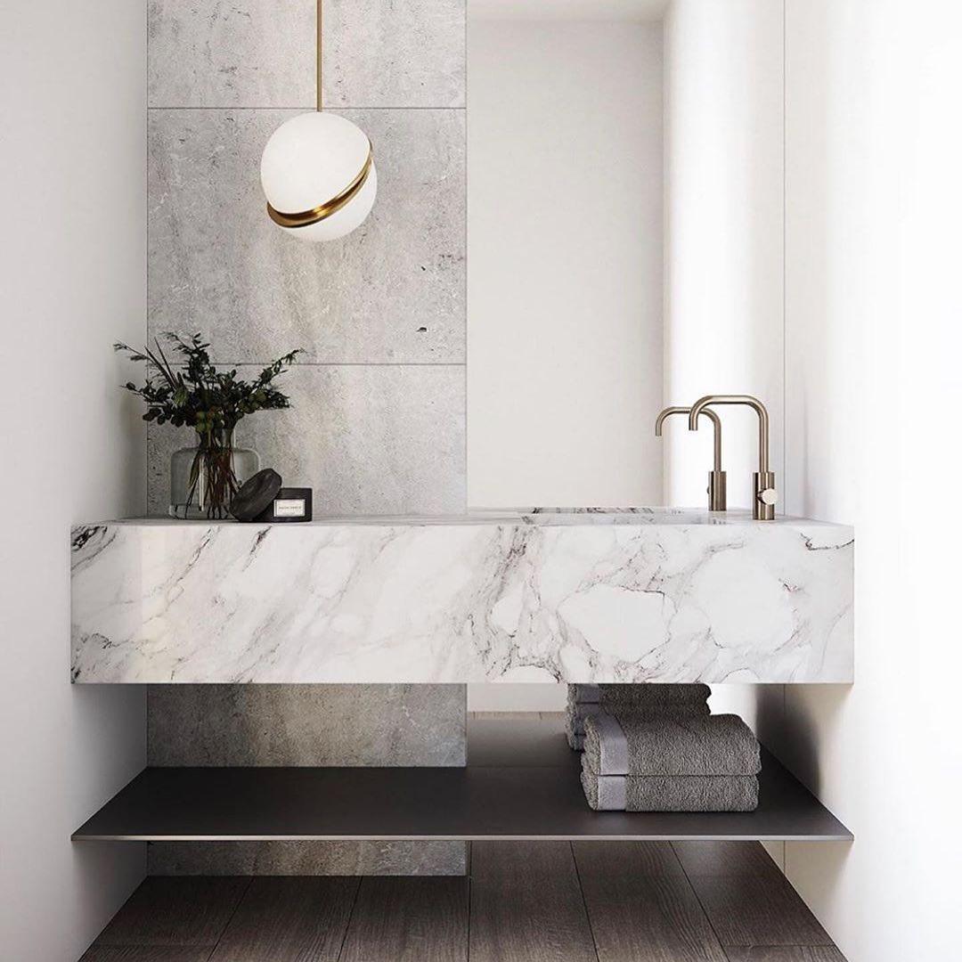 Above a marble vanity with brass tapware, a single pendant glows from this Clérachic fixture.