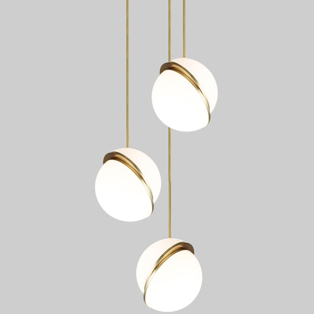 Against a mid-grey backdrop, three opal spheres with brass crescents descend in a column, from Clérachic.