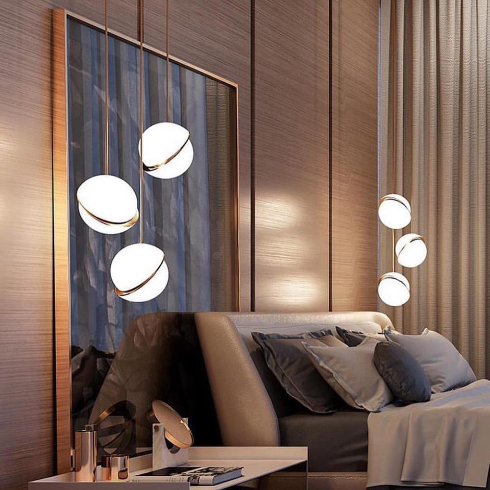 Three of this Clérachic pendant trail from brass rods above a bed, set against a warm wood-panelled headboard wall.