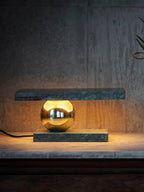 Clérachic green marble table lamp glowing against a dark backdrop, set on a stone surface with its cord trailing off.