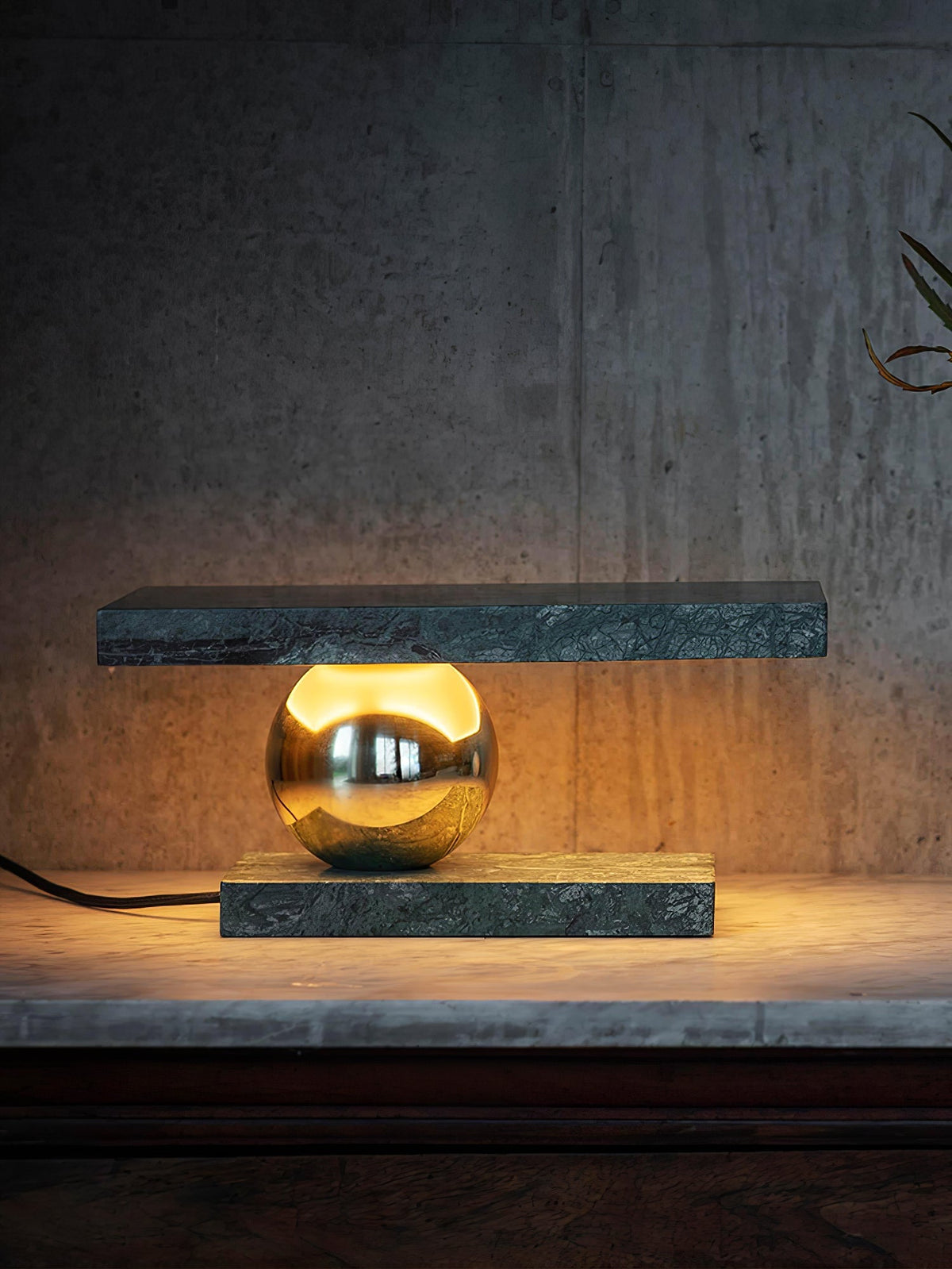 Clérachic green marble table lamp glowing against a dark backdrop, set on a stone surface with its cord trailing off.