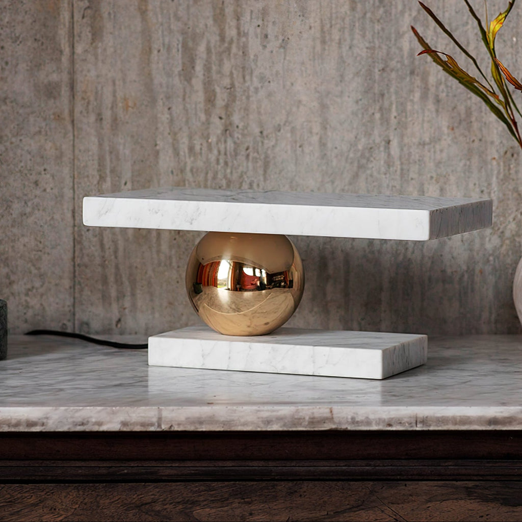 Clérachic white marble table lamp glowing on a marble surface in a softly lit living room, cord resting alongside.